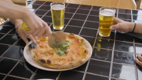 Vista-Superior-De-La-Mano-De-Un-Comensal-Cortando-Pizza-En-Una-Mesa-De-Restaurante