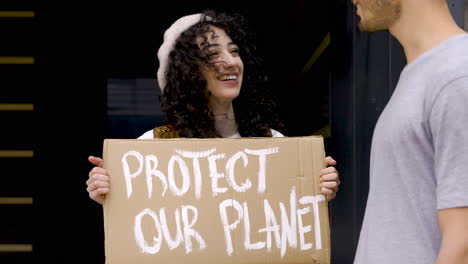 Joven-Hablando-Con-Una-Joven-Sosteniendo-Proteger-Nuestro-Tablero-Planetario-Para-Protestar