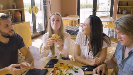 Group-Of-Four-Happy-Friends-Sharing-Pizza-And-Talking-At-Restaurant