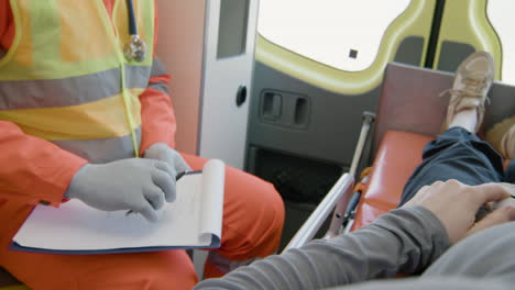 Close-Up-View-Of-A-Patient-Lying-On-A-Stretcher-Inside-An-Ambulance-While-A-Paramedic-Taking-Notes-In-Medical-Report