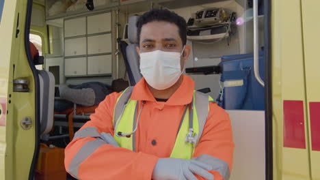 Portrait-Of-A-Latin-Male-Paramedic-With-Crossed-Arms-And-Face-Mask-Standing-In-Front-Of-An-Ambulance-And-Looking-At-The-Camera