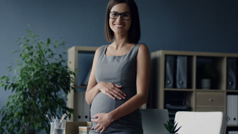 Schwangere-Geschäftsfrau,-Die-Ihren-Bauch-Streichelt-Und-In-Die-Kamera-Lächelt