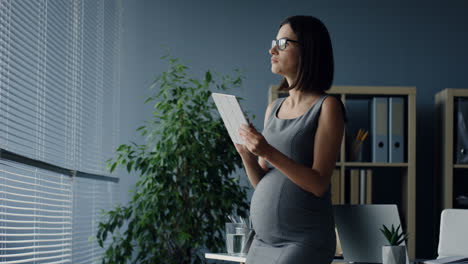 Mujer-De-Negocios-Embarazada-Usando-Una-Tableta-Mientras-Bebe-Agua-En-La-Oficina