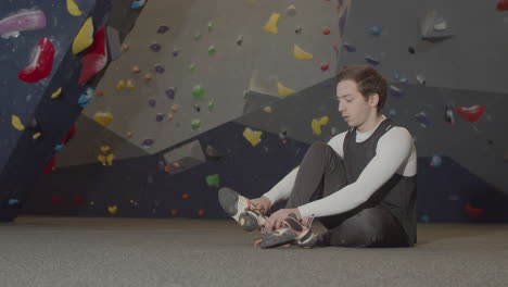 Young-Male-Athlete-Sitting-In-Bouldering-Gym-And-Putting-Climbing-Shoes-On
