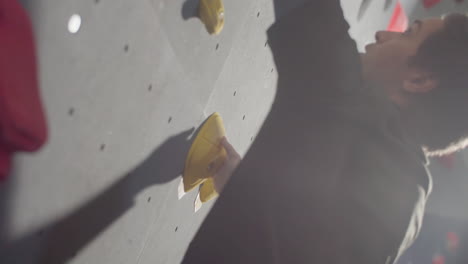Vertical-Close-Up-Shot-Of-A-Young-Male-Athlete-Climbing-Artificial-Rock-Wall-In-Bouldering-Gym