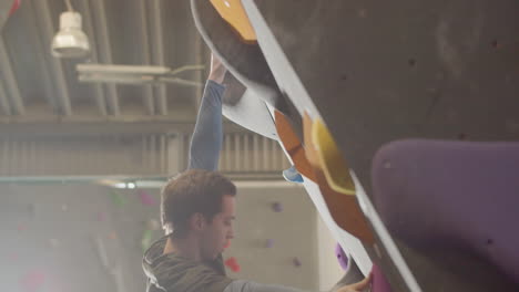 Low-Angle-Shot-Of-A-Strong-Male-Athlete-Climbing-Artificial-Rock-Wall-In-Bouldering-Gym