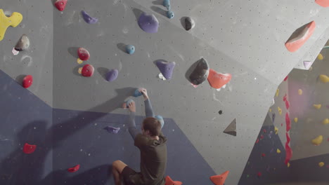 Low-Angle-Shot-Of-A-Strong-Male-Athlete-Climbing-Artificial-Rock-Wall-In-Bouldering-Gym-1