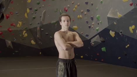 Medium-Shot-Of-A-Young-Shirtless-Sportsman-Standing-In-Bouldering-Gym-And-Looking-At-The-Camera