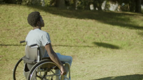 Side-View-Of-Young-Black-Man-In-Wheelchair-Enjoying-Ride-In-Park