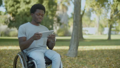 Junger-Schwarzer-Mann-Im-Rollstuhl-Verbringt-Zeit-Im-Freien-Mit-Tablet