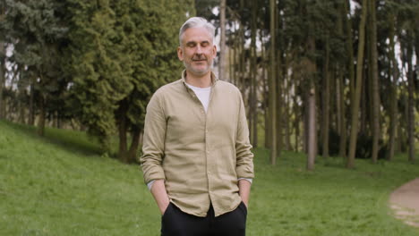 Portrait-Of-A-Gray-Haired-Man-Standing-In-The-Park-With-His-Hands-In-Pockets-And-Looking-At-The-Camera