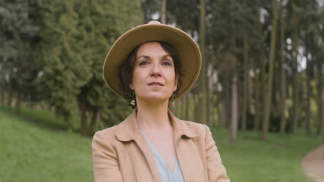 Portrait-Of-A-Middle-Aged-Woman-In-Hat-Standing-In-The-Park-And-Looking-At-The-Camera