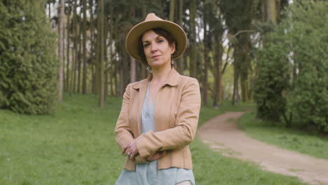 Portrait-Of-A-Middle-Aged-Woman-In-Hat-And-Crossed-Arms-Standing-In-The-Park-And-Looking-At-The-Camera