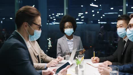 Multiethnische-Geschäftsleute-Gruppieren-Sich-In-Medizinischen-Masken-Bei-Einem-Teammeeting-In-Einem-Modernen-Büro-Und-Diskutieren-über-Ein-Projekt