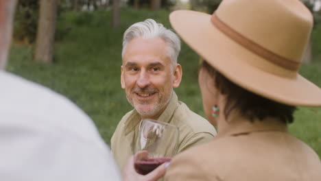 Gray-Haired-Man-Talking-With-A-Woman-Who-Drinking-Red-Wine-During-An-Outdoor-Party-In-The-Park