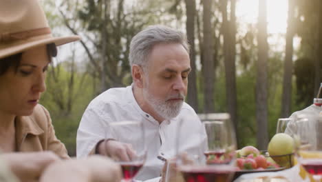 Middle-Aged-Man-Eating-And-Talking-To-His-Friends-Sitting-At-Table-During-An-Outdoor-Party-In-The-Park