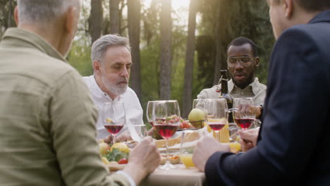 Group-Of-Middle-Aged-Friends-Eating-And-Talking-To-Each-Other-Sitting-At-Table-During-An-Outdoor-Party-In-The-Park-1