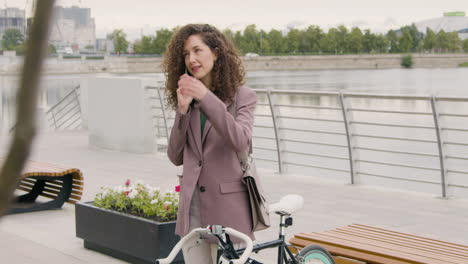 Curly-Woman-In-Formal-Clothes-And-Bicyle-Talking-On-Mobile-Phone-On-The-City-Bridge-1