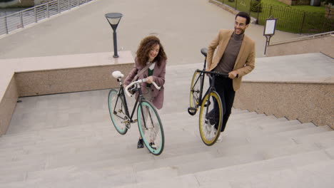 American-Man-And-Woman-In-Formal-Clothes-Carrying-Their-Bikes-Up-The-Stairs-While-Going-To-Work