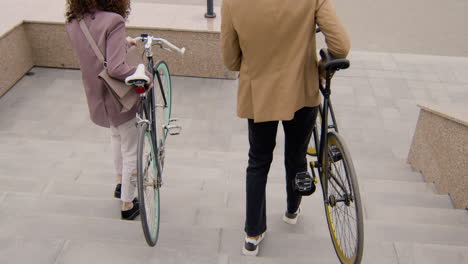 Vista-Trasera-De-Un-Hombre-Y-Una-Mujer-Americanos-Con-Ropa-Formal-Llevando-Sus-Bicicletas-Por-Las-Escaleras-Mientras-Van-Al-Trabajo