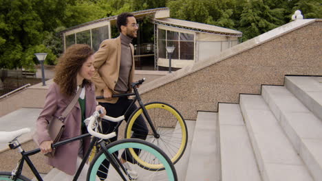 Side-View-Of-American-Man-And-Woman-In-Formal-Clothes-Carrying-Their-Bikes-Up-The-Stairs-While-Going-To-Work