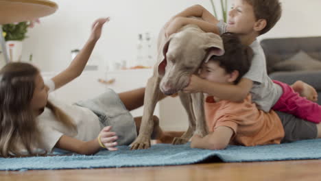 Glückliche-Kinder,-Die-Auf-Dem-Boden-Liegen-Und-Zu-Hause-Mit-Dem-Hund-Spielen