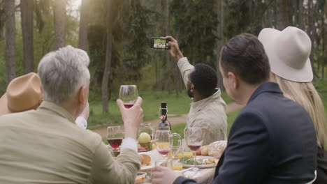 Group-Of-Middle-Aged-Friends-Taking-A-Selfie-Sitting-At-Table-During-An-Outdoor-Party-In-The-Park