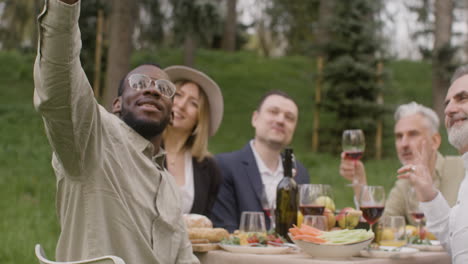 Group-Of-Middle-Aged-Friends-Taking-A-Selfie-Sitting-At-Table-During-An-Outdoor-Party-In-The-Park-1