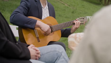 Unerkennbarer-Mann,-Der-Gitarre-Spielt-Und-Mit-Seinen-Freunden-Während-Einer-Party-Im-Park-Im-Freien-Am-Tisch-Sitzt