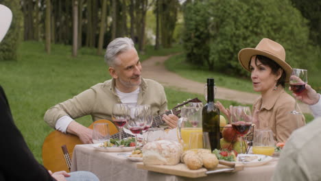 Middle-Aged-Man-Plating-A-Guitar-Sitting-At-Table-With-His-Friends-During-An-Outdoor-Party-In-The-Park-1