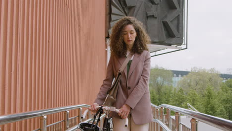 Pretty-Curly-Woman-In-Formal-Clothes-Walking-To-The-Office-With-Her-Bike
