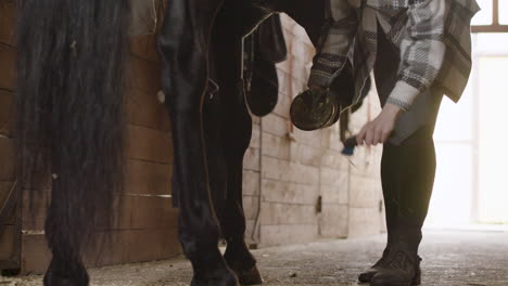 Female-Jockey-Cleaning-Horse's-Hoof-And-Horseshoe
