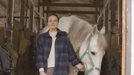 Weißes-Pferd,-Das-Heu-Frisst,-Während-Ihr-Besitzer-Für-Die-Kamera-Posiert-Und-Sie-Hält