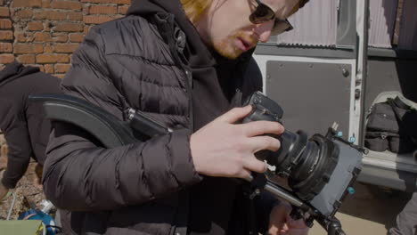 Close-Up-View-Of-Redheaded-Production-Worker-In-Wool-Cap-And-Sunglasses-Setting-Up-A-Camera-In-The-Street