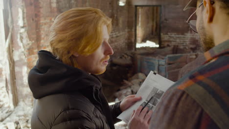 Close-Up-View-Of-Two-Production-Coworkers-Talking-And-Reading-A-Document-About-The-Movie-In-A-Ruined-Building-1