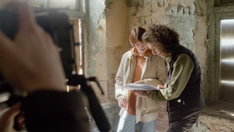 Coworkers-Reading-A-Script-In-A-Ruined-Building-While-They-Are-Being-Recorded-By-A-Cameraman-1