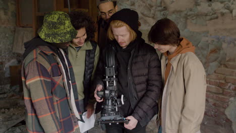 Production-Team-And-Cameraman-Reviewing-A-Scene-In-A-Camera-In-A-Ruined-Building