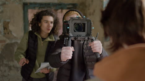 Production-Worker-And-Cameraman-Closely-Recording-A-Girlâ€šÃ„Ã´s-Face-During-A-Scene-In-A-Ruined-Building