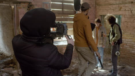 Cameraman-And-Team-Production-Recording-A-Movie-Scene-With-A-Redheaded-Girl-And-Man-Wearing-Black-Balaclava-In-A-Ruined-Building