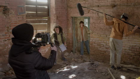 Close-Up-View-Of-A-Cameraman-Recording-A-Scene-Of-A-Redhead-Girl-Running-Away-From-A-Man-In-A-Black-Balaclava-In-A-Ruined-Building