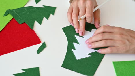 Female-hands-cut-out-a-christmas-tree-of-green-fabric-with-scissors-using-a-template