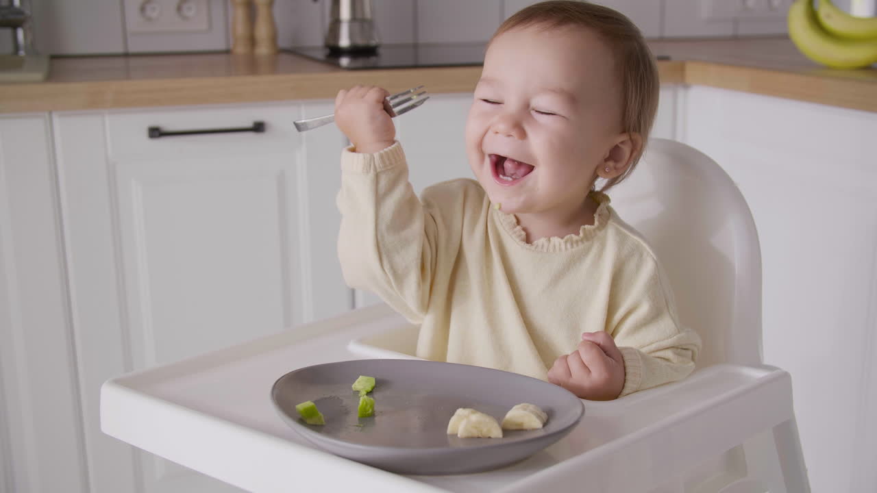 Free stock video Cute baby girl eating avocado slice using fork while