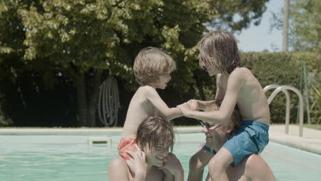 Two-boys-sitting-on-father-and-brother's-necks-and-having-fun-in-the-swimming-pool
