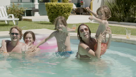 Glückliche-Familie,-Die-In-Die-Kamera-Winkt,-Während-Sie-Sich-Entspannt-Und-Spaß-Im-Schwimmbad-Hat