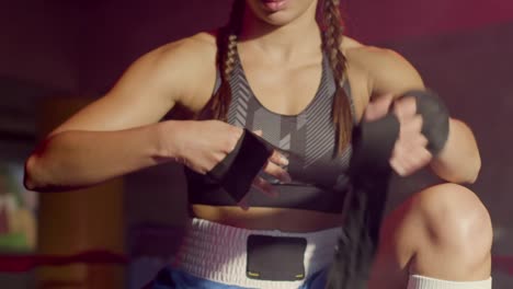 Young-Caucasian-sportswoman-with-braided-pigtails-wrapping-hands-with-boxing-bandages-at-gym