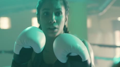 Close-up-shot-of-a-strong-Caucasian-sportswoman-training-with-coach,-wearing-boxing-gloves-and-punching-boxing-paws