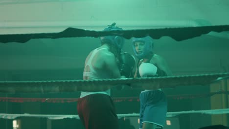 Two-female-boxers-in-helmets-and-boxing-gloves-fighting-in-ring-at-gym