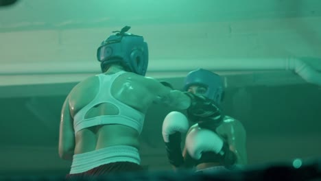Two-female-boxers-in-helmets-and-boxing-gloves-fighting-in-ring-at-gym
