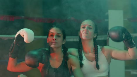 Two-confident-female-boxers-in-braided-pigtails-sitting-near-the-ring,-looking-at-the-camera-and-showing-biceps
