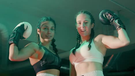 Two-smiling-female-boxers-in-braided-pigtails-looking-at-the-camera-and-showing-biceps